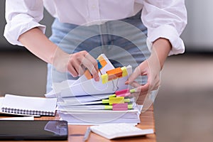 Hand of a businesswoman working for searching in Stacks of paper documents on wooden desks at the workplace