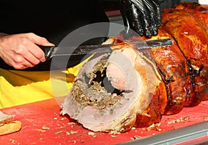 hand of a butcher in a black glove cuts slices of porchetta a flavorful pork salume photo
