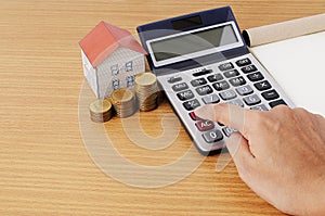 Hand on calculator with coins stack and paper house for mortgage