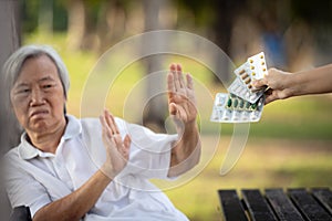 Hand of caregiver giving medicine pills and capsules to the elderly,asian senior woman refusing to take medication,afraid,bad side photo