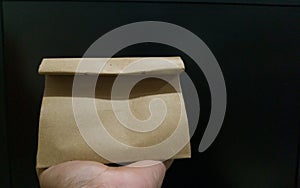 A hand carrying small paper bag with black background