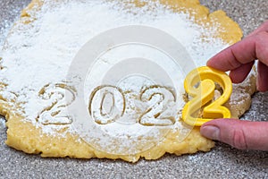 Hand carving from raw dough sprinkled with white flour like snow the date 2022 for New Year& x27;s and Christmas cookies.