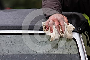 Hand of a caucasian man holding a cloth and cleaning or drying the wheel arch and headlamp of a classic car after rain