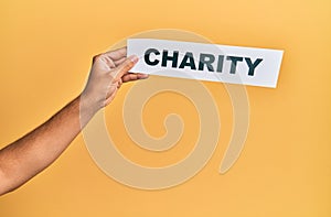 Hand of caucasian man holding paper with charity word over isolated yellow background