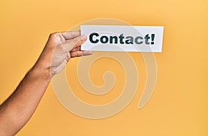 Hand of caucasian man holding paper with contact! word over isolated yellow background