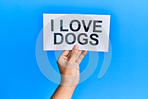 Hand of caucasian man holding paper with i love dogs message over isolated blue background