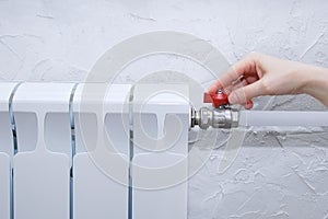 The hand of a Caucasian woman turns tap valve on a heating radiator