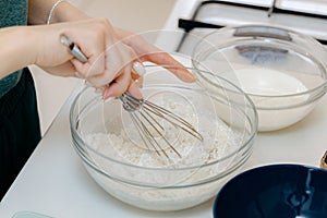 The hand of a Caucasian young girl mixes the dough with a whisk in a bowl.