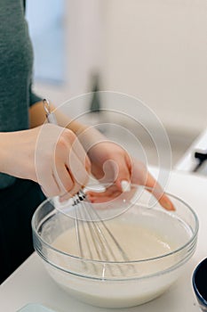 The hand of a Caucasian young girl mixes the dough with a whisk in a bowl.