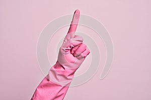 Hand of caucasian young man with cleaning glove over isolated pink background counting number one using index finger, showing idea