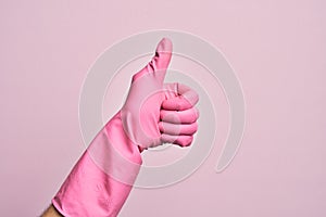Hand of caucasian young man with cleaning glove over isolated pink background doing successful approval gesture with thumbs up,