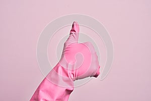 Hand of caucasian young man with cleaning glove over isolated pink background doing successful approval gesture with thumbs up,