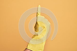Hand of caucasian young man with cleaning glove over isolated yellow background counting number one using index finger, showing