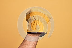 Hand of caucasian young man with gardener glove over isolated yellow background doing protest and revolution gesture, fist