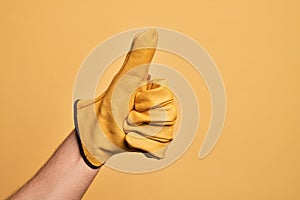 Hand of caucasian young man with gardener glove over isolated yellow background doing successful approval gesture with thumbs up,