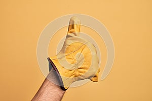 Hand of caucasian young man with gardener glove over isolated yellow background doing successful approval gesture with thumbs up,