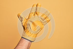 Hand of caucasian young man with gardener glove over isolated yellow background greeting doing Vulcan salute, showing back of the