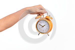 Hand of caucasian young man holding yellow vintage alarm clock over isolated white background