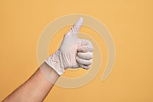 Hand of caucasian young man with medical glove over isolated yellow background doing successful approval gesture with thumbs up,