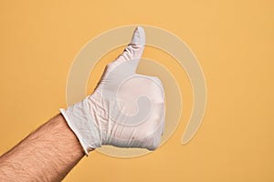 Hand of caucasian young man with medical glove over isolated yellow background doing successful approval gesture with thumbs up,