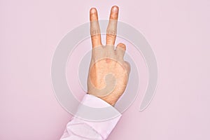 Hand of caucasian young man showing fingers over isolated pink background counting number 2 showing two fingers, gesturing victory