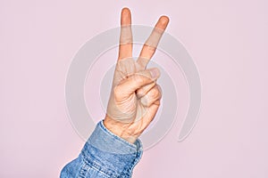 Hand of caucasian young man showing fingers over isolated pink background counting number 2 showing two fingers, gesturing victory