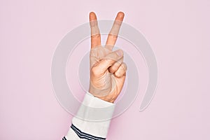 Hand of caucasian young man showing fingers over isolated pink background counting number 2 showing two fingers, gesturing victory