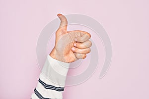 Hand of caucasian young man showing fingers over isolated pink background doing successful approval gesture with thumbs up,