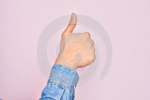 Hand of caucasian young man showing fingers over isolated pink background doing successful approval gesture with thumbs up,