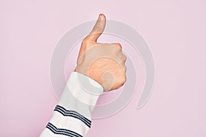 Hand of caucasian young man showing fingers over isolated pink background doing successful approval gesture with thumbs up,