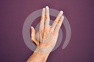 Hand of caucasian young man showing fingers over isolated purple background greeting doing Vulcan salute, showing back of the hand