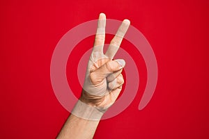 Hand of caucasian young man showing fingers over isolated red background counting number 2 showing two fingers, gesturing victory
