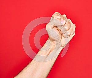 Hand of caucasian young man showing fingers over isolated red background doing protest and revolution gesture, fist expressing