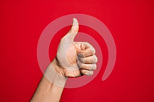 Hand of caucasian young man showing fingers over isolated red background doing successful approval gesture with thumbs up,