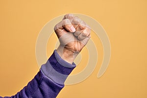 Hand of caucasian young man showing fingers over isolated yellow background doing protest and revolution gesture, fist expressing