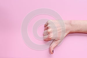 Hand of a caucasian young woman doing gesture of thumbs down on a pink background