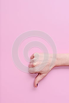 Hand of a caucasian young woman doing gesture of thumbs down on a pink background