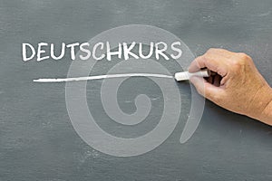 Hand on a chalkboard with the German word Deutschkurs (German co