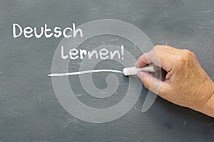 Hand on a chalkboard with the German words Deutsch lernen (Learn