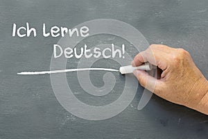 Hand on a chalkboard with the German words Ich lerne Deutsch (I