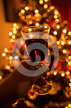 Hand cheering with red wine glass against out of focus christmas tree lights, xmas festive celebration concept
