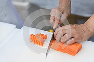 Hand of chef use knife preparing a fresh salmon on a cutting board, Japanese chef in restaurant slicing raw salmon, ingredient for