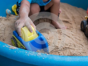 Hand of child boy playing car toy in sandbox outdoor.