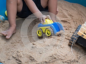 Hand of child boy playing car toy in sandbox outdoor.