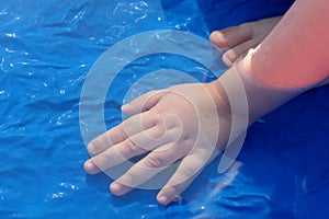 Hand of a child dipped in water of blue plastic swimming pool