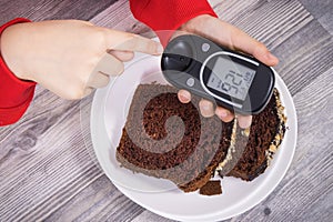 Hand of child holding glucose meter with result sugar level, sweet chocolate cake. Nutrition during diabetes