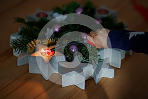 Hand of child lighting a candle on advent wreath on Christmas eve or first advent. Tradtional wreath in Germany. Happy