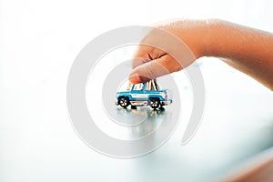 Hand of a child playing with a small blue car toy on a smooth background