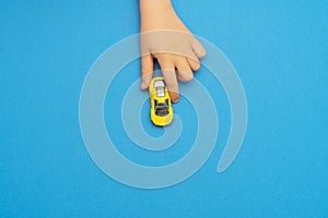 Hand of child playing with small yellow toy car on blue background, copy space