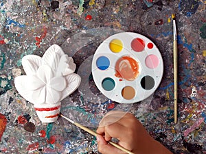 hand of children painting frangipani plumeria flower plaster with paint brush and colorful palette